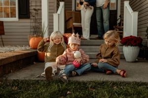 Children sitting on front porch steps surrounded by fall decorations and pumpkins.