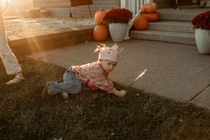 Child laying in grass at sunset wearing fairy wings near pumpkin decorated steps.