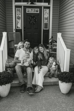 Family portrait on front porch steps with black door and decorative planters.
