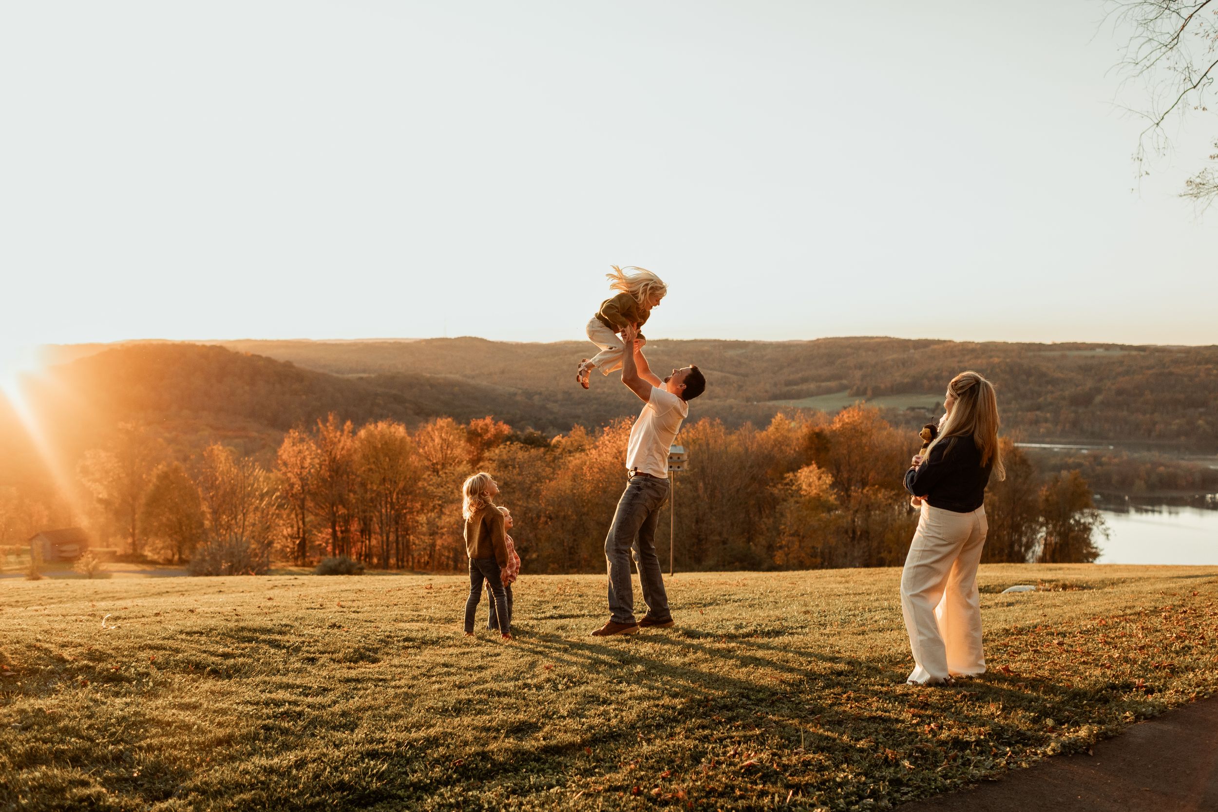 Family playing together on grassy hill during golden hour sunset.