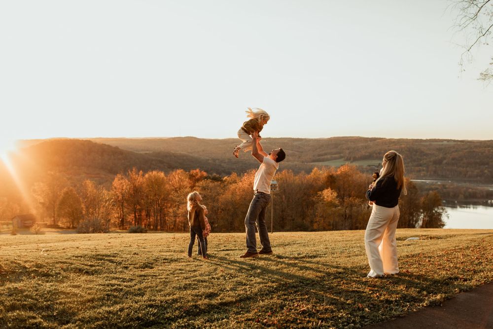 Family playing together on grassy hill during golden hour sunset.