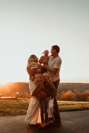 Family embracing outdoors during golden sunset with rolling hills in background.