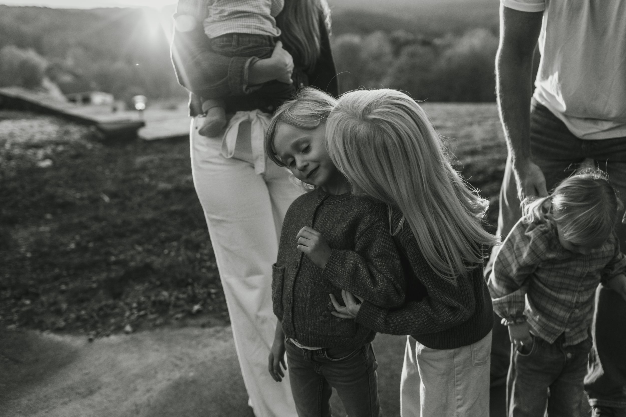 Black and white candid photo of family members hugging outdoors.