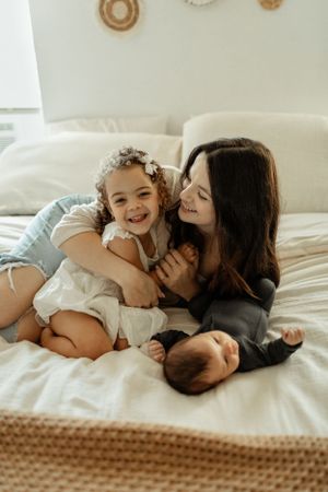 Warm family moment captured on white bedding with decorative wall accents visible.