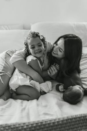 Intimate black and white photograph of family members sharing a tender moment on white bedding.