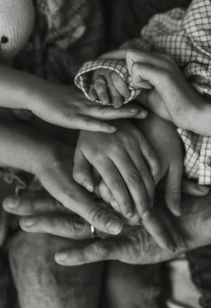 Black and white close-up of multiple hands tenderly touching in an intimate family moment.