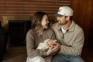 Couple sharing tender moment in warm sweaters against brick wall background.
