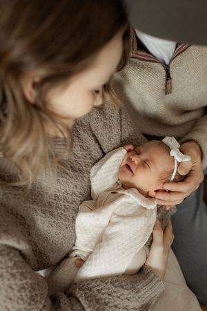 A tender moment as a newborn baby in a white outfit with a bow is held and cradled in soft natural lighting.