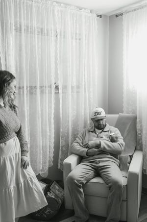 A black and white photo of a quiet moment in a room with sheer curtains and a reclining chair.