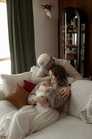 A cozy family moment on a white couch with soft natural light streaming through green curtains.