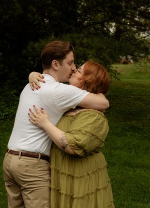 Couple sharing a kiss while embracing outdoors on a lush green lawn in summer.