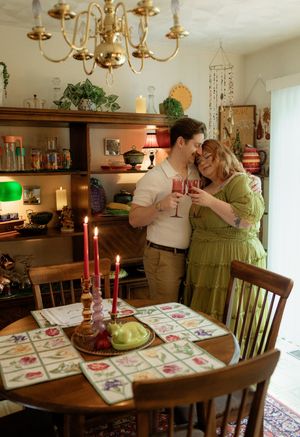 Couple sharing a romantic toast with pink drinks by candlelight in a cozy, eclectic dining room.