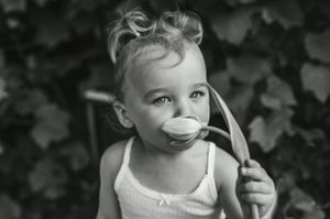 Black and white photo of a toddler with a pacifier looking up at the camera.