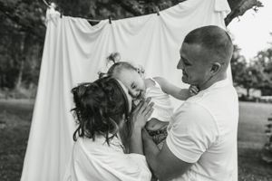 Black and white outdoor family portrait against white backdrop showing tender interaction.