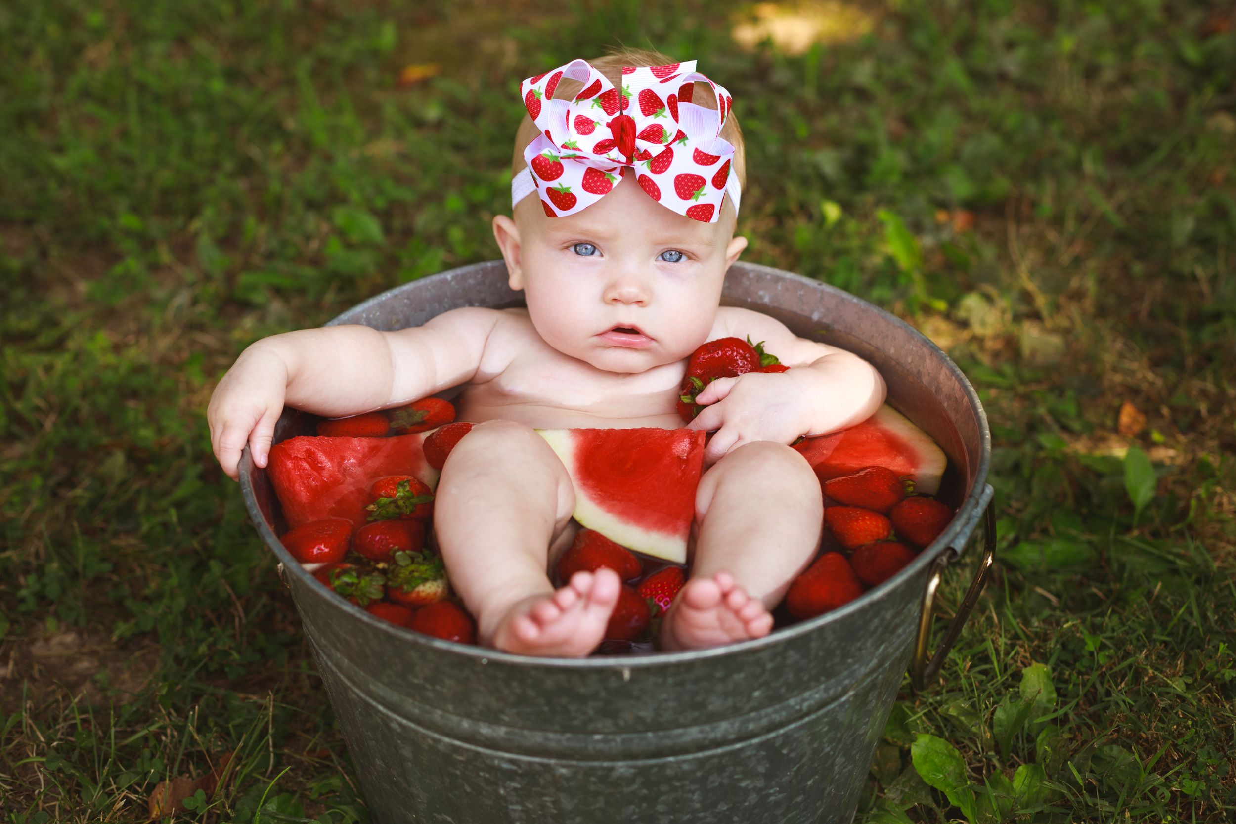 Baby girl in a strawberry and watermelon bath with cute strawberry bow on her head.