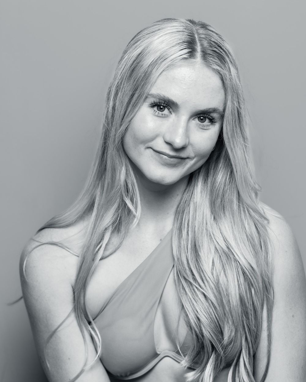 Black and white portrait of a young woman with long blonde hair smiling softly in a studio.