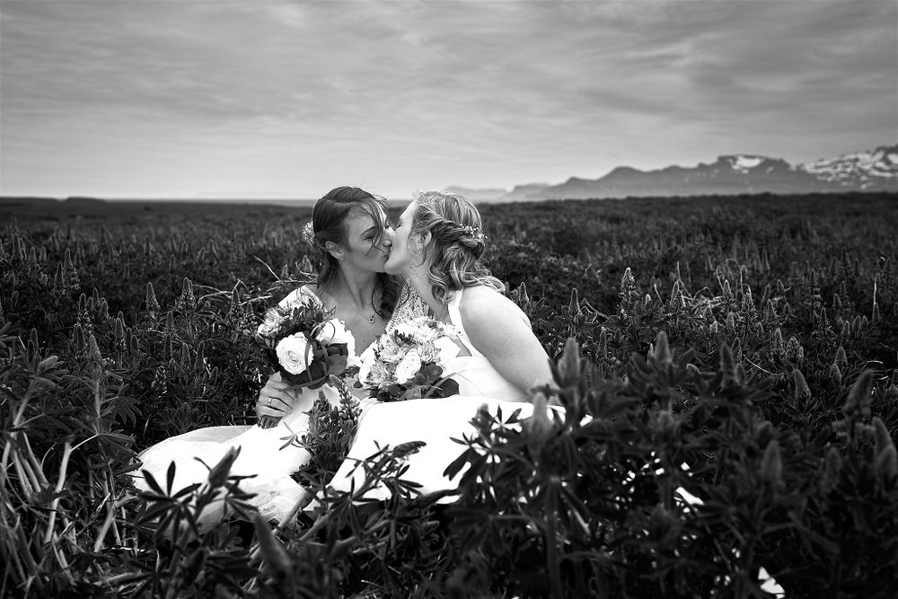 A black and white photo of two brides laughing together in a wildflower field.