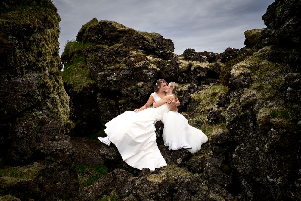A dramatic wedding portrait framed by rocky cliffs with white dresses flowing in the wind.