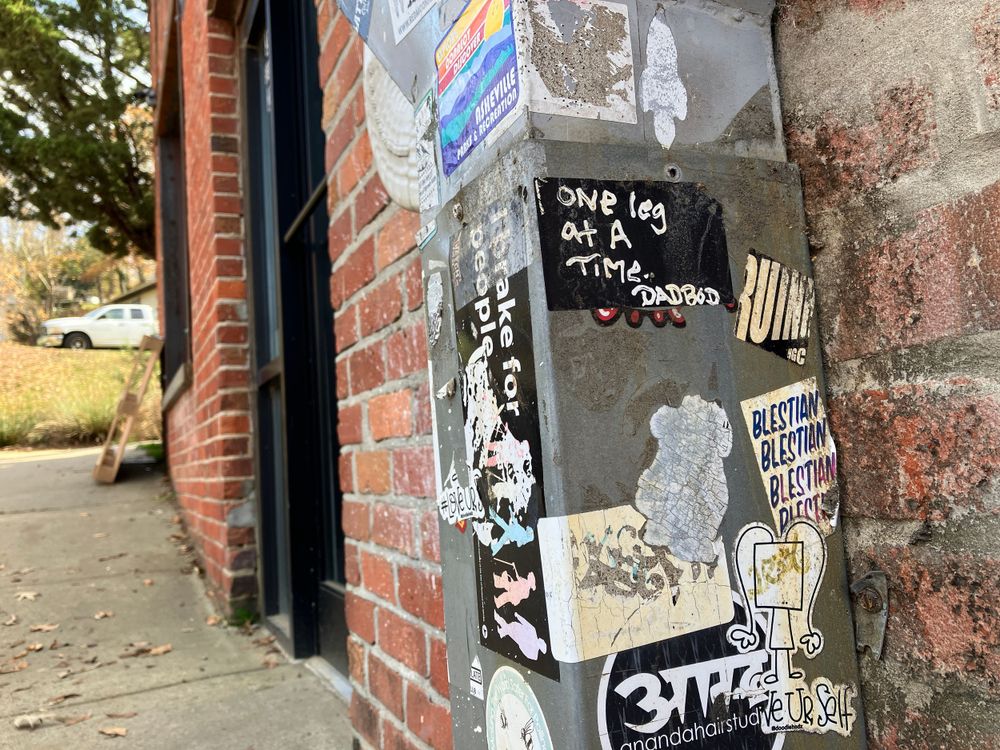 Close-up of graffiti stickers and street art on a weathered brick wall corner.