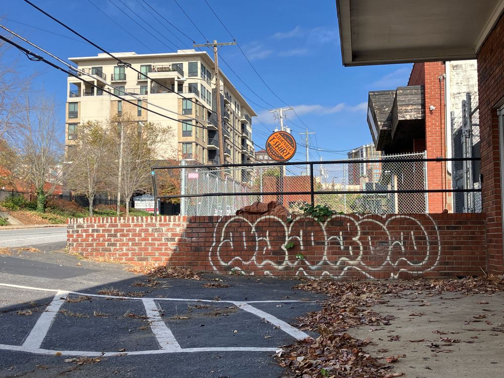 Urban parking lot with graffiti on brick wall and apartment building in background under blue sky.
