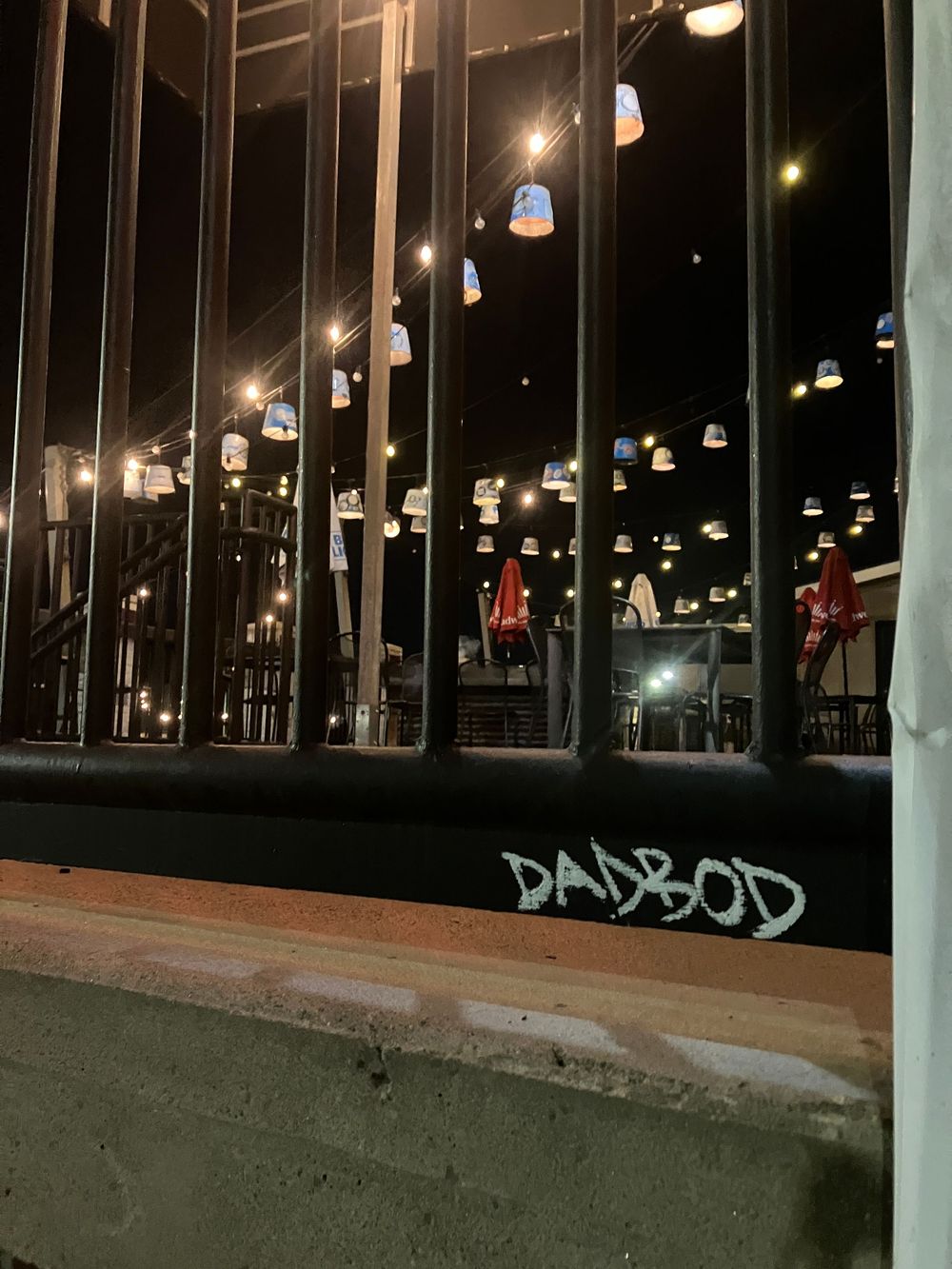 Illuminated hanging lights reflect in glass windows at night with graffiti visible at the bottom.