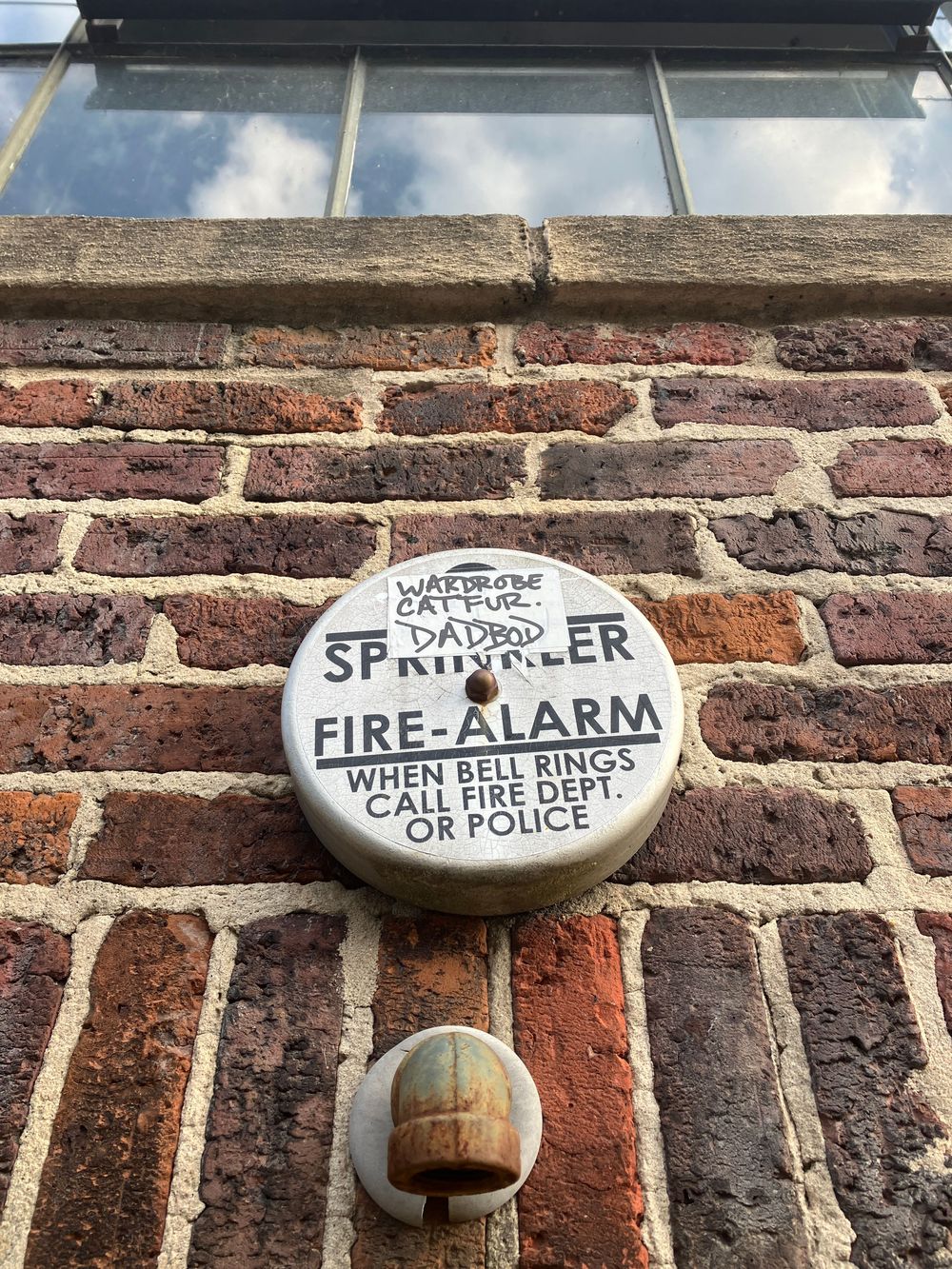 Vintage fire alarm and sprinkler system controls mounted on weathered brick wall with painted white text labels.