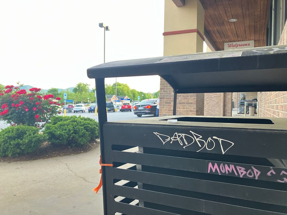 A row of black awnings with pink and white graffiti text extends along the exterior of a commercial building.