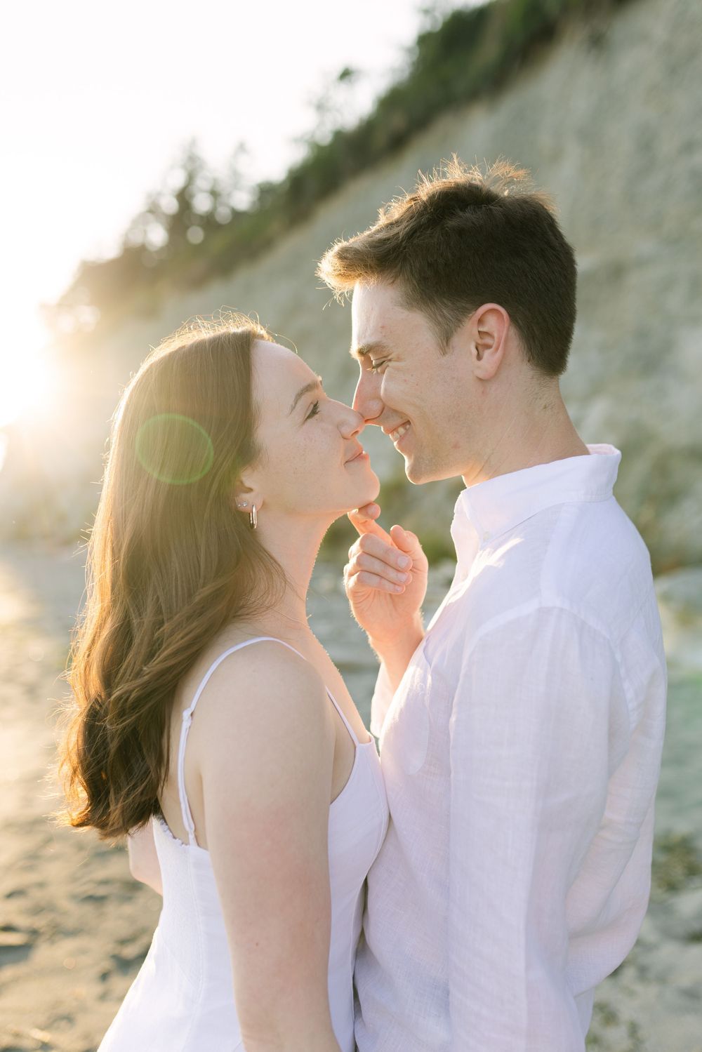 A romantic couple shares intimate moments on a sunlit beach with white cliffs in the background.