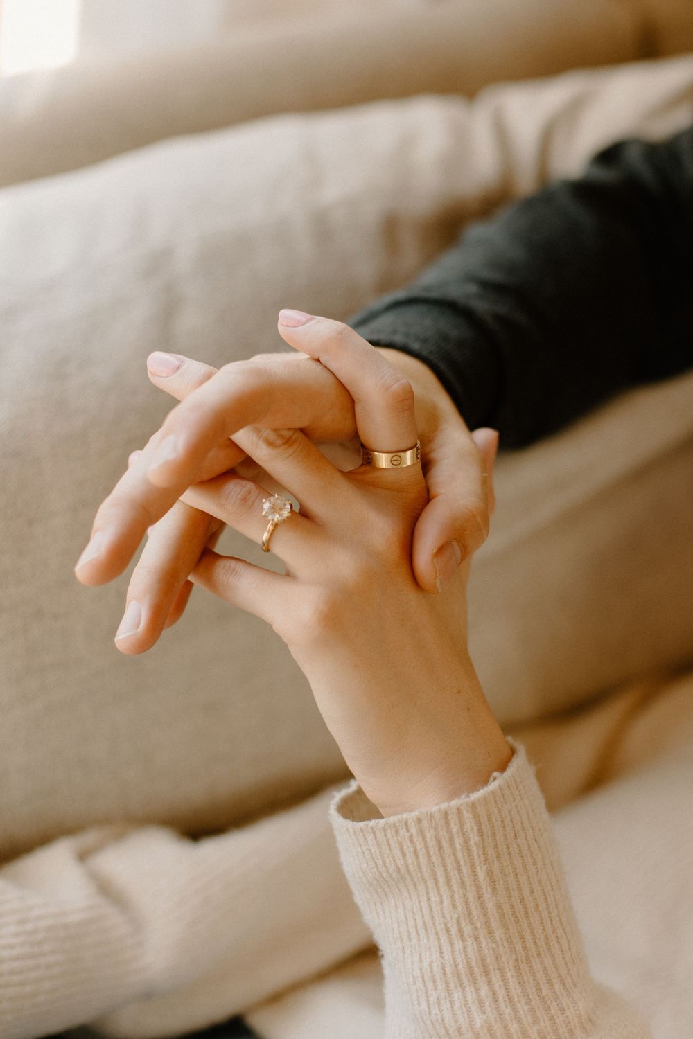Close-up of intertwined hands showing wedding rings against a soft beige background.