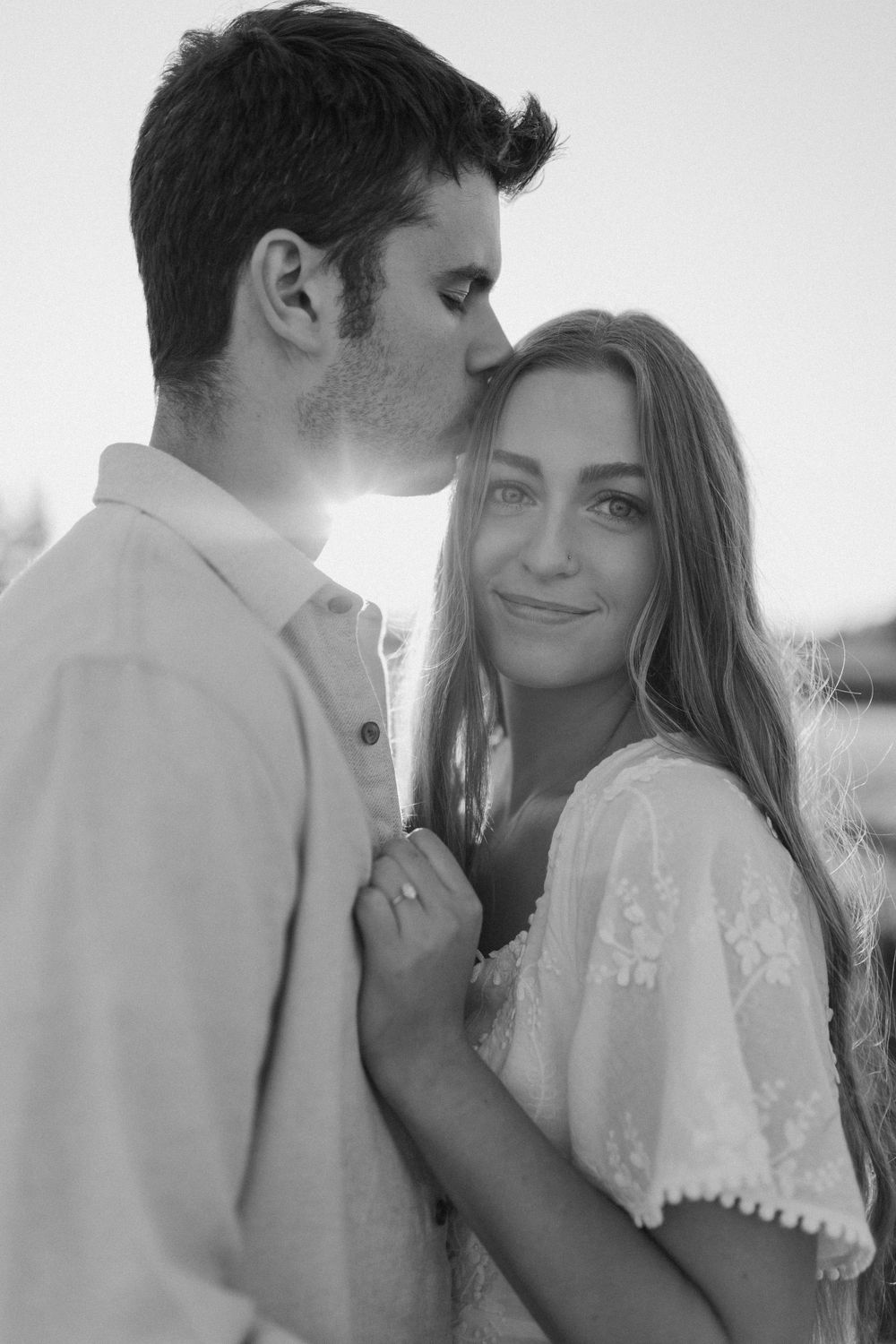 An intimate black and white portrait of a couple sharing a tender moment in natural light.