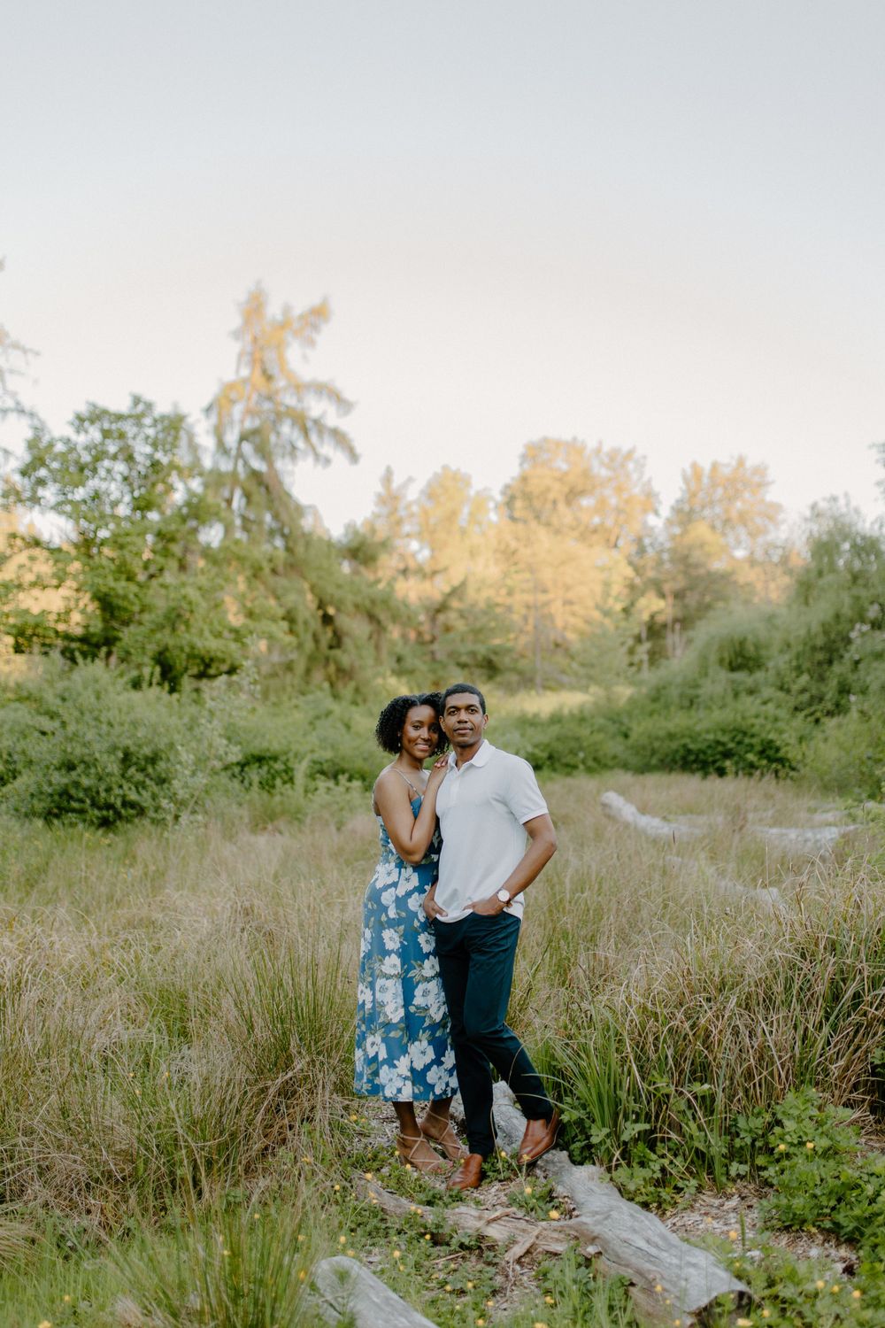 A couple stands together in a field during golden hour wearing coordinated blue and white outfits.