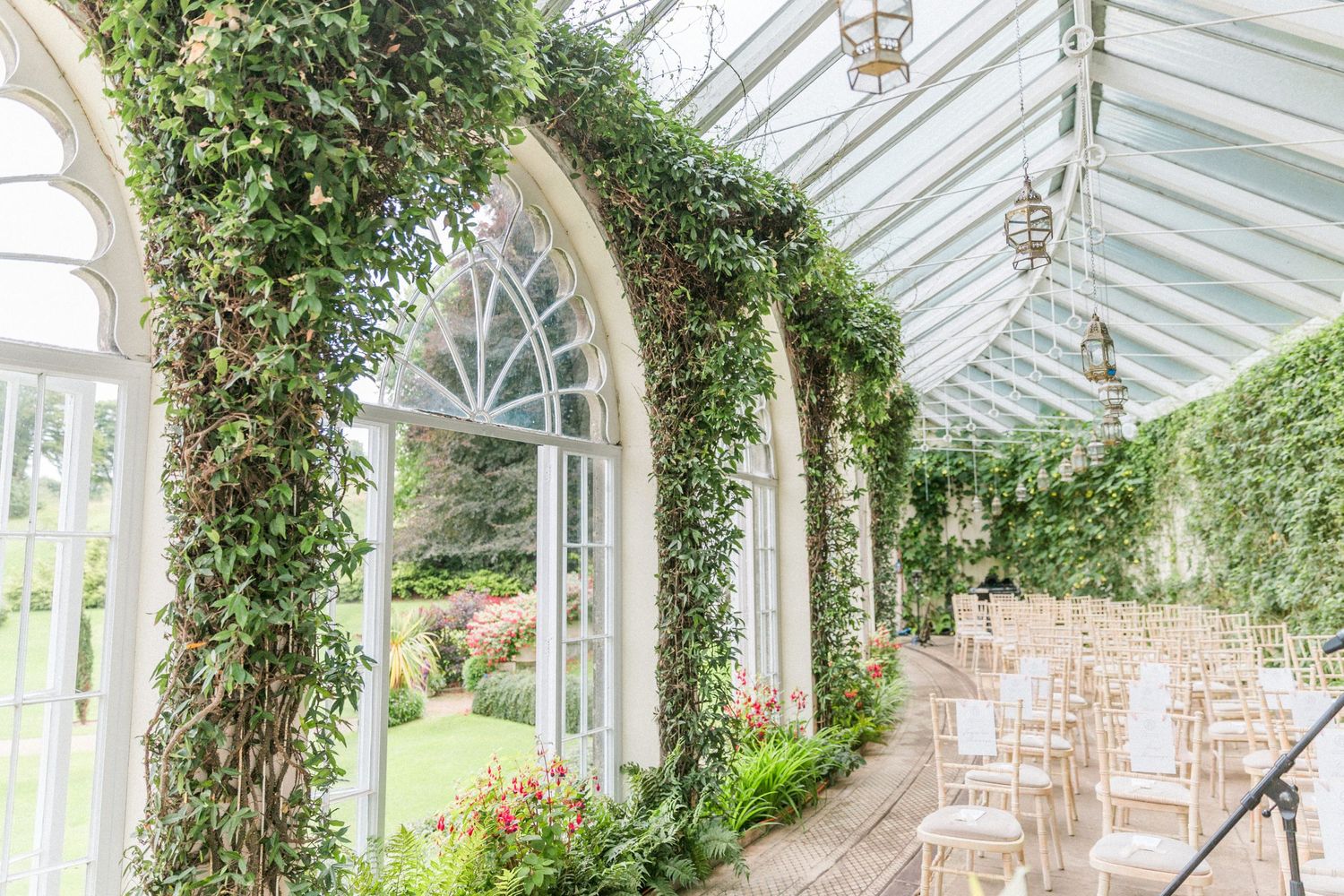 Elegant oratory wedding venue sezincote house with white arched windows, climbing ivy vines, and white chairs set up for a ceremony.