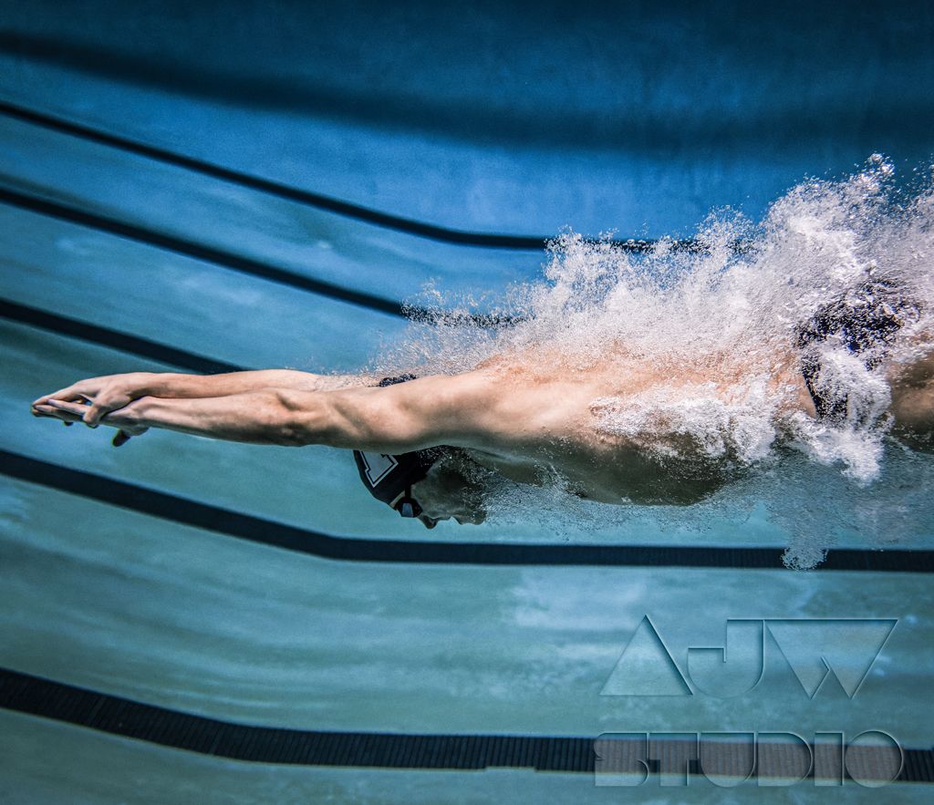 Swimmer diving through water with perfect form creating dramatic splash in pool lane.