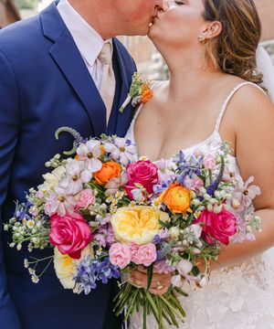 A vibrant bridal bouquet with pink, yellow and orange roses alongside purple delphinium and white flowers.