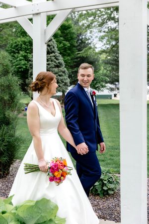 A couple shares a joyful moment under a white pergola during their outdoor garden wedding celebration.