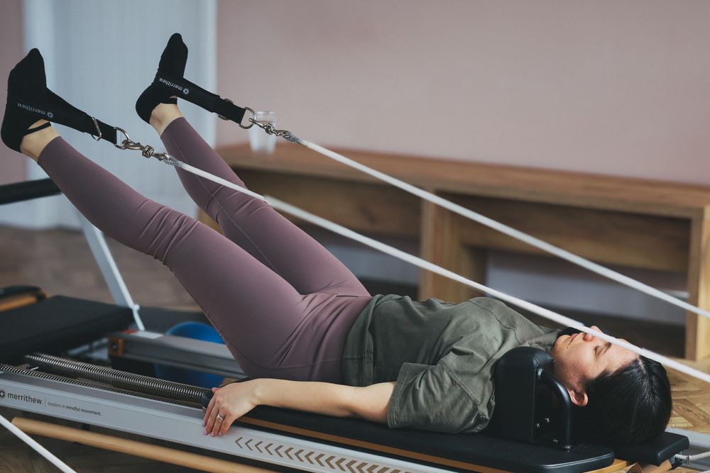 Woman lying on Pilates reformer machine performing leg exercise in studio.