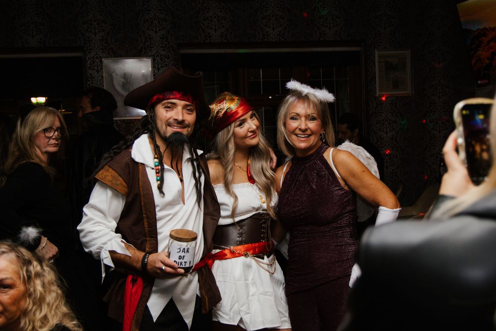 Three people in Halloween costumes including a pirate and two angels posing together at a party.