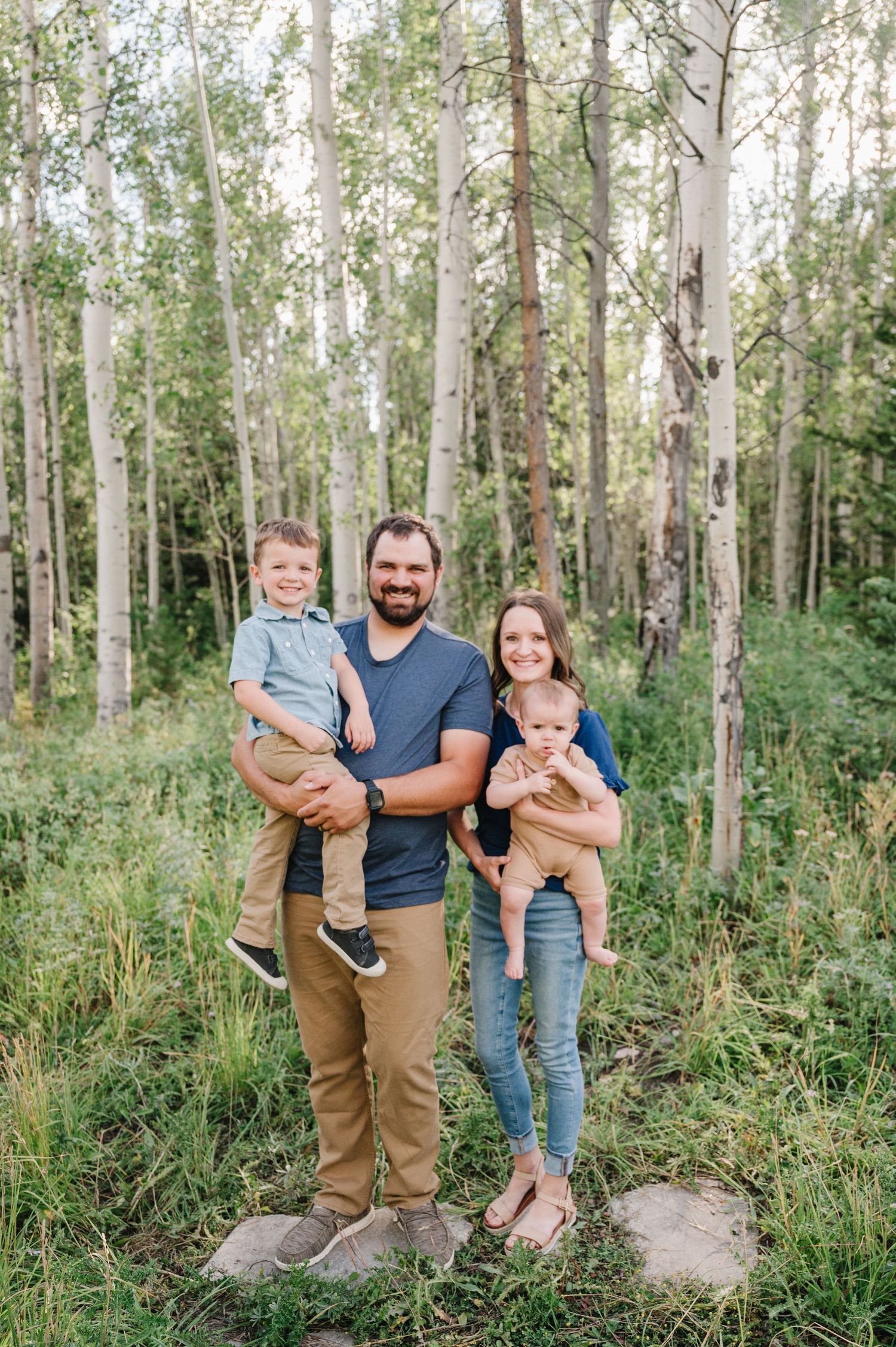 A family of four poses together in a scenic aspen forest setting.