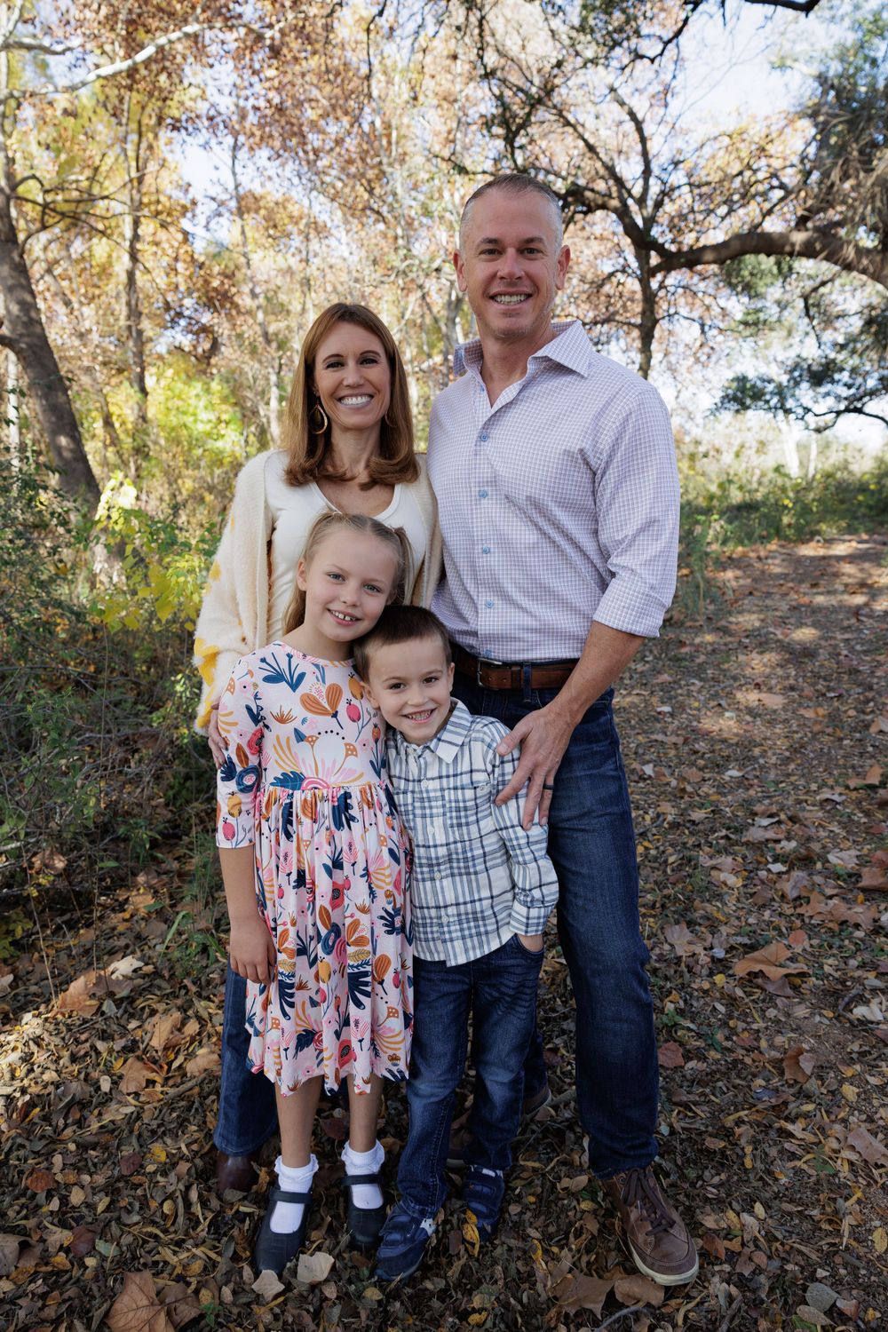 A family of four poses together among fall foliage in an outdoor setting.