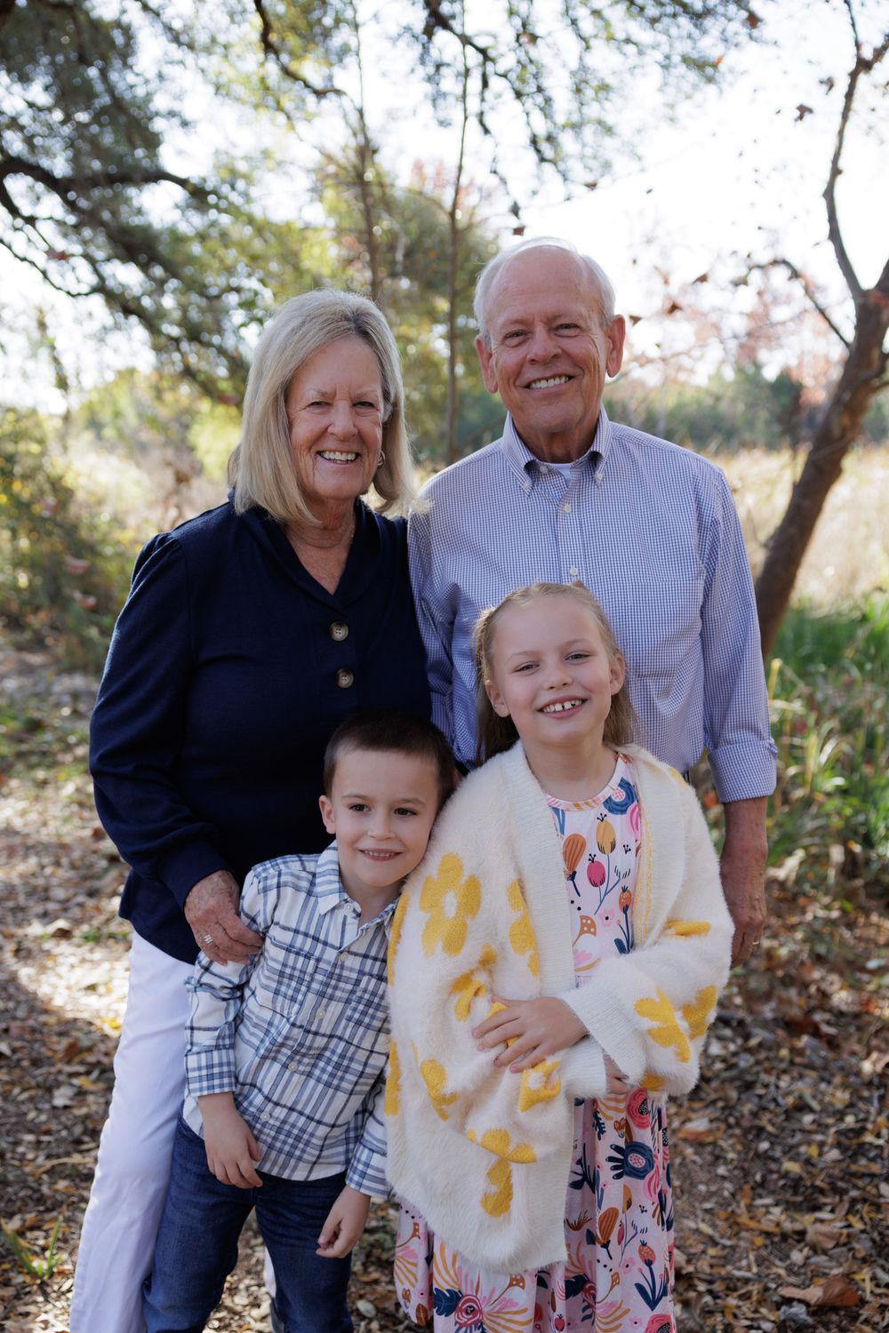 A family group poses together outdoors with autumn trees in the background.