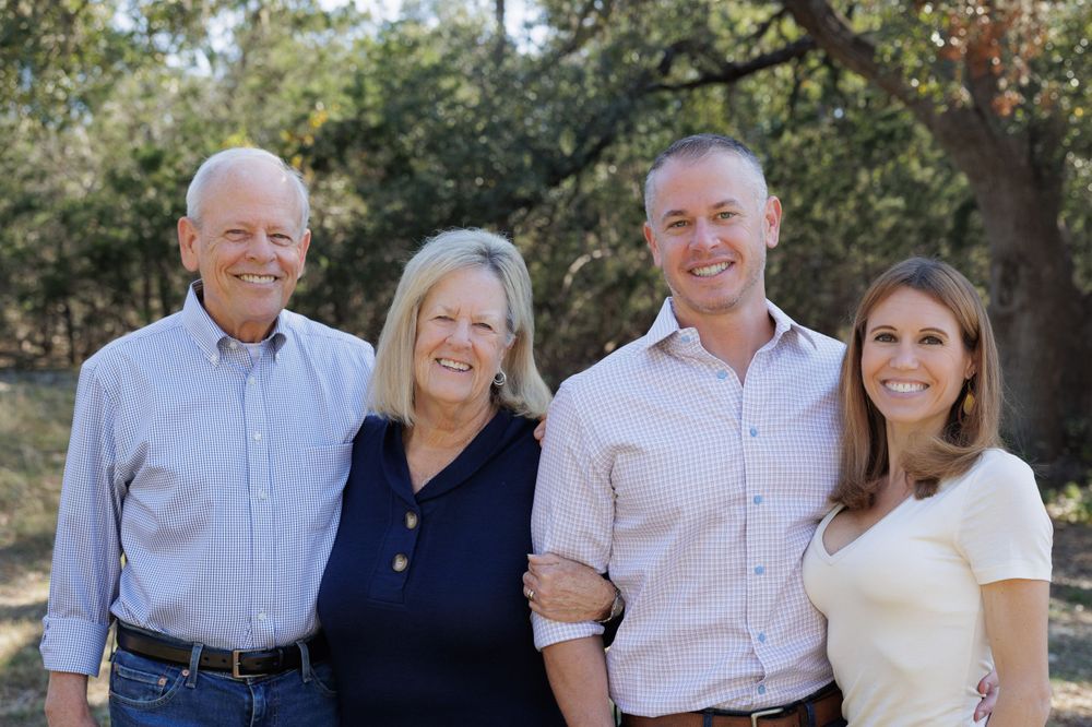 Family of four poses together outdoors with trees in background.