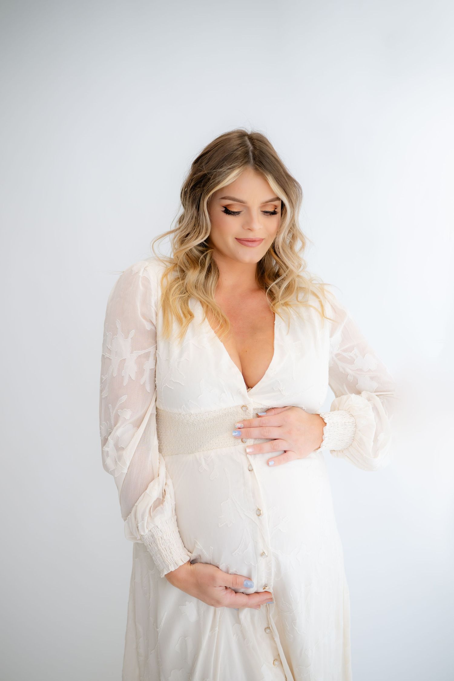 Studio maternity portrait in elegant white button-down dress against light background.