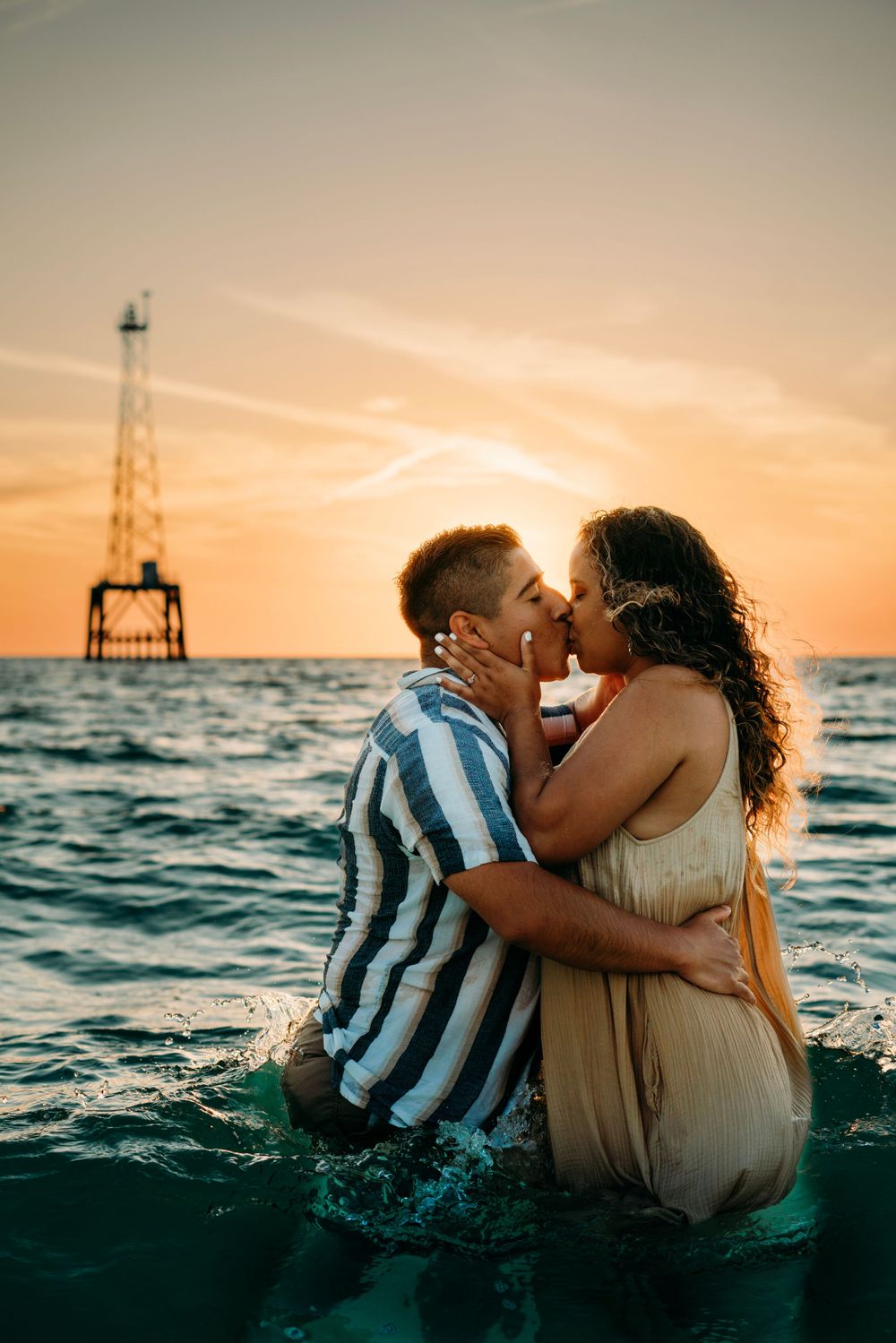 Husband and wife in water kissing at sunset.