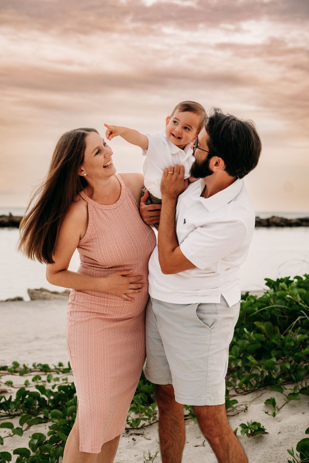 Mother and father holding toddler pointing in distance.