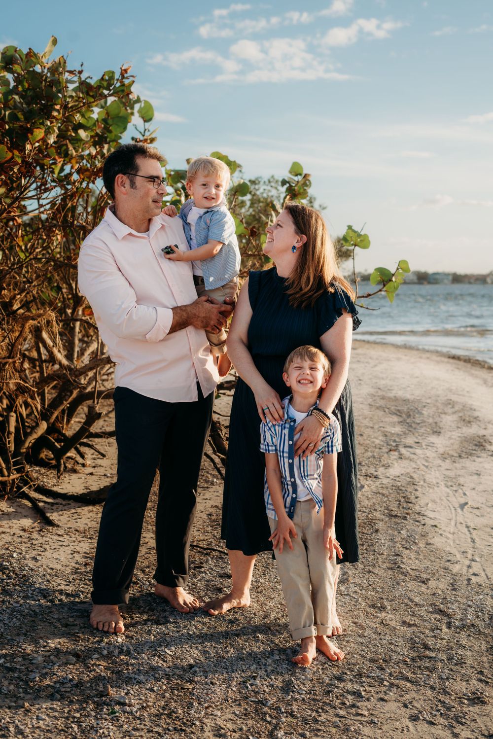 Family of four smiling and looking at each other in a beach setting.