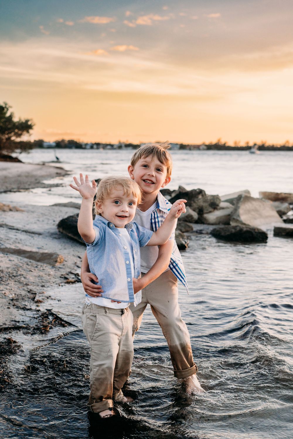 Two brothers posing for the camera together in a beach setting with water and rocks.