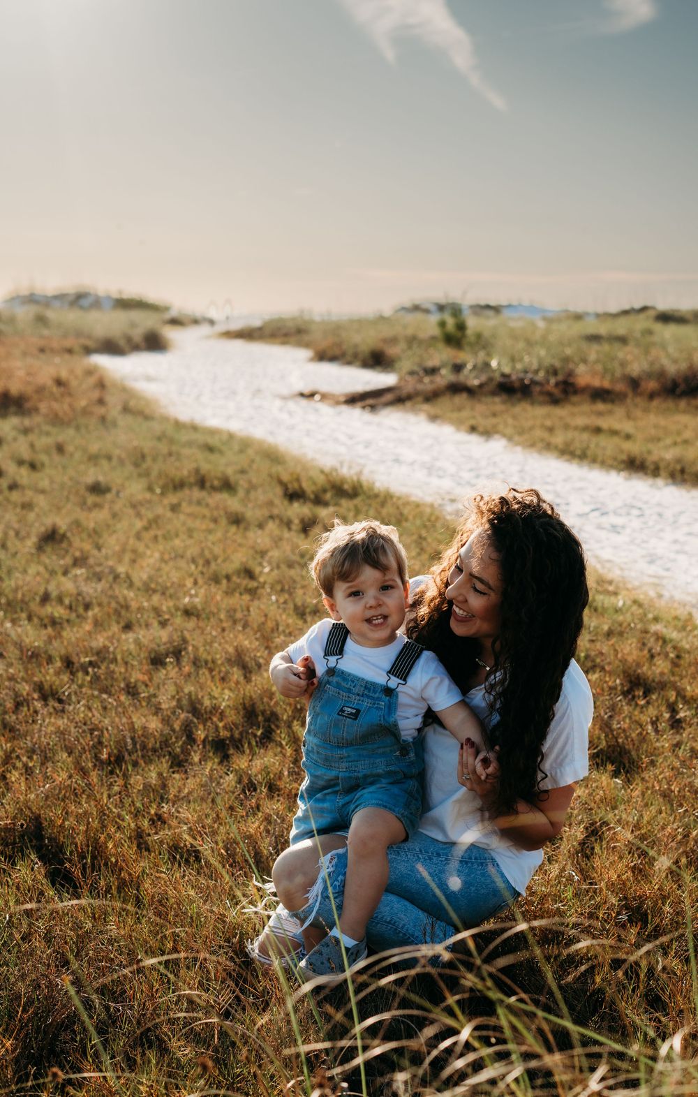 Mother and son smiling at the end of a beach trail surrounded by greenery.