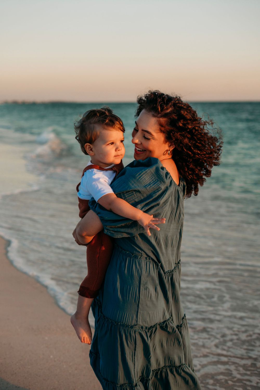 Mother holding and dancing with son at the beach.