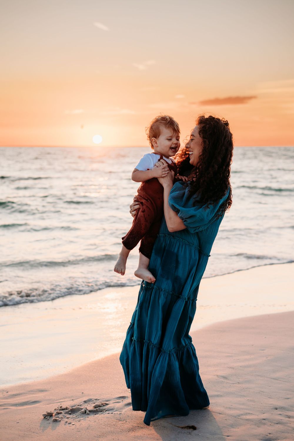 Mother dancing with son at sunset on the beach.