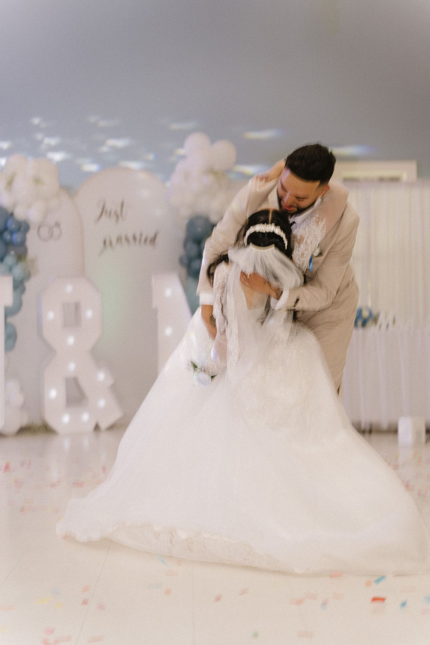 Newlywed couple sharing a romantic dip dance in front of a Just Married balloon backdrop at their wedding.